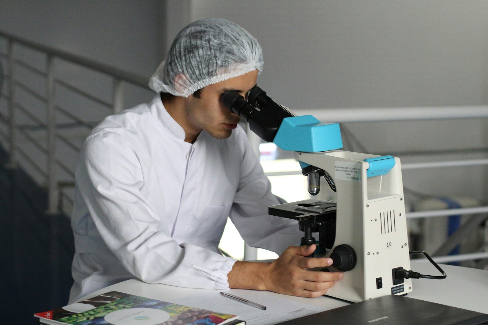 A researcher in a lab coat examines a sample under a microscope, highlighting the focus on scientific study and analysis in a laboratory setting.
